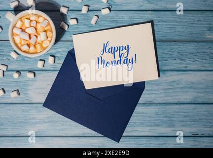 HAPPY MONDAY blauer Montag Concept Text blauer Umschlag mit weißer Tasse Kaffee und Marshmallows auf hölzernem Hintergrund. Die meisten Absteiger Stockfoto