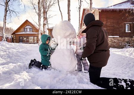 Eine Familie baut im Winter einen Schneemann aus weißem Schnee auf dem Hof. Stockfoto