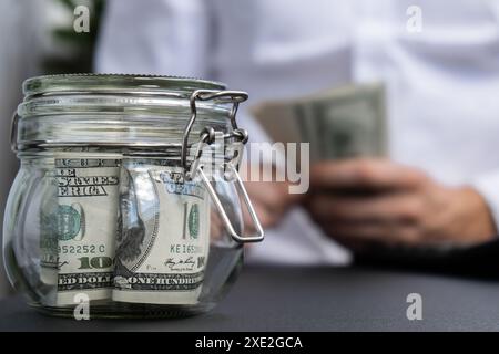Dollar-Banknote Spart Geld Im Glasglas. Nicht erkennbarer Mensch berechnet Geld auf Rechner gemäßigter Konsum und Wirtschaft Col Stockfoto