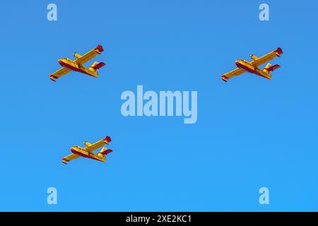 Gijon, Spanien - 24. Mai 2024: Drei leuchtend gelbe und rote Löschflugzeuge fliegen in Formation gegen einen klaren blauen Himmel Stockfoto