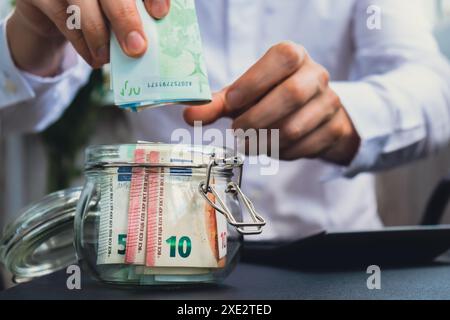 Euro-Banknote Spart Geld Im Glasgefäß. Unerkennbarer Mann moderat Konsum auf Rechner und Wirtschaft sammeln Geld Tipps Stockfoto