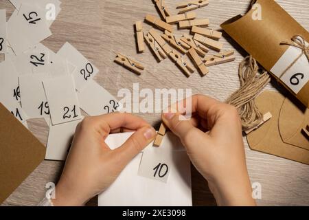 Unerkennbare junge Frau klebt Nummer auf Basteltasche, schließt sie mit Kleiderschrank. Frau, die Kraftpapier für selbstgemachte Adventszeit herstellt Stockfoto