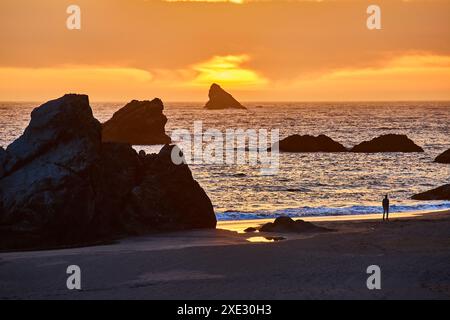 Einsame Figur am Sunset Beach mit Felsformationen in der Golden Hour Stockfoto