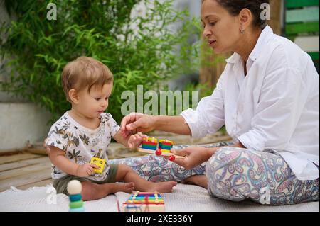 Eine Frau spielt mit einem Baby mit pädagogischem Spielzeug und fördert das Lernen und Binden in einer grünen Umgebung im Freien. Stockfoto