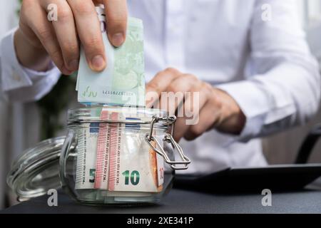 Euro-Banknote Spart Geld Im Glasgefäß. Unerkennbarer Mann moderat Konsum auf Rechner und Wirtschaft sammeln Geld Tipps Stockfoto