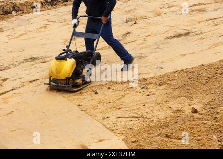 Arbeiter mit Vibrationsplattenverdichter zum Verdichten von Sand während der Pfadkonstruktion. Stockfoto