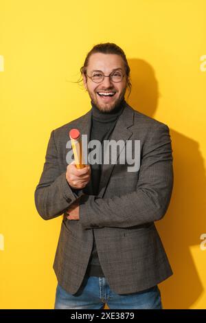 Fröhlicher Mann, der eine Brille trägt und große Penci auf gelbem Hintergrund hält Stockfoto