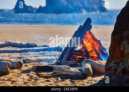 Lagerfeuer am Strand bei Sonnenuntergang mit Blick auf das Meer aus der Perspektive auf Augenhöhe Stockfoto