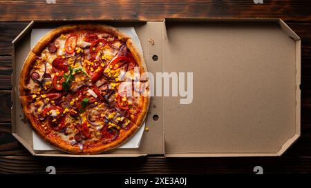 Peperoni Pizza mit Paprika, Zuckermais und Rucola in offener Schachtel auf dunklem Holztisch flach Stockfoto