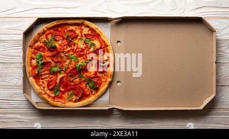 Peperoni Pizza mit Paprika und Rucola in offener Schachtel auf weißem Holzküchentisch flach Stockfoto