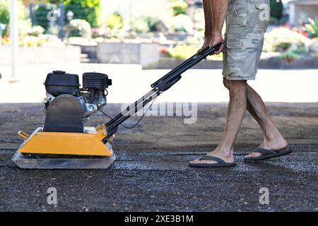 Arbeitskraft mit Vibrationsplattenverdichter, um den Boden am Arbeitsplatz zu festigen. builder , komprimiert zerquetschte Stk Stockfoto
