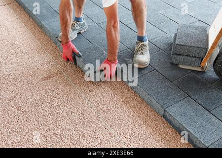 Blockieren Sie die Pflastersteine auf Sand mit einer Fadenlinie, und legen Sie die Kanten an. Hände eines Pflasterarbeiters, Stockfoto