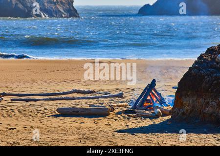 Lagerfeuer am mit Treibholz übersäten Strand bei Sonnenuntergang - Perspektive auf Augenhöhe Stockfoto