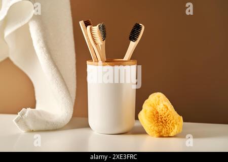 Bambus-Zahnbürsten in einer Tasse und ein Handtuch im Badezimmer. Stockfoto