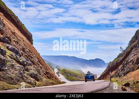 Küstenstraßenabenteuer mit Blue Car und der Perspektive der rauen Klippen auf Augenhöhe Stockfoto