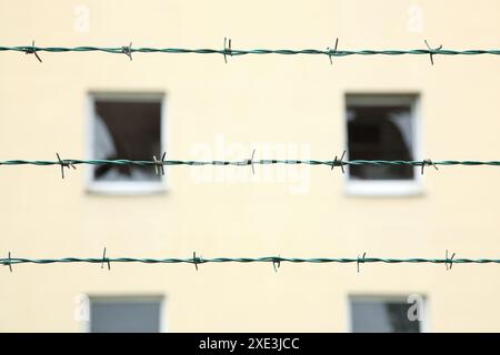 Reihen von Stacheldraht vor einem verlassenen Wohngebäude mit gebrochenen Fenstern Hintergrund. Geister Stockfoto