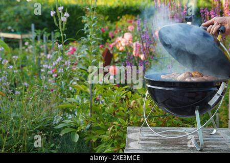 Barbecue Grill, köstliche Schweinebratwürste und gegrilltes Fleisch über den Kohlen auf dem Grill. Die Hand des Mannes ist Stockfoto