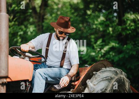 Mann mit Hut, der einen Traktor in ländlicher Umgebung bei sonnigem Wetter fährt Stockfoto