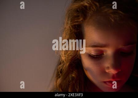 Mädchen mit langen braunen Haaren und pinkfarbenen Lippen, die nach unten schauen, nachdenken, nachdenken, mit dem Licht, das von der Seite auf sie scheint und im Kopierraum Stockfoto