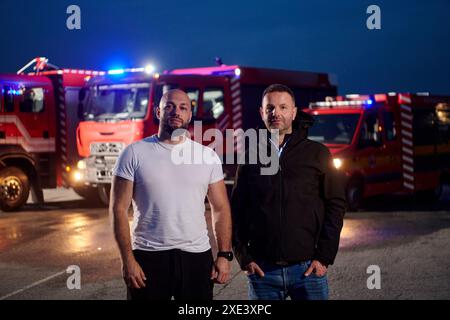 Eine Gruppe von Feuerwehrleuten, die in Zivilkleidung gekleidet sind, steht nachts vor Feuerwehrfahrzeugen und zeigt einen Moment des Cama Stockfoto