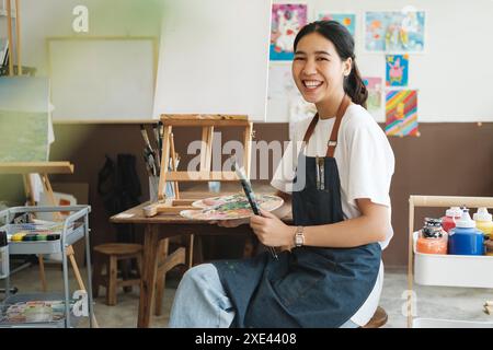 Junge asiatische Künstlerin im Atelier schaut in die Kamera und lächelt. Stockfoto