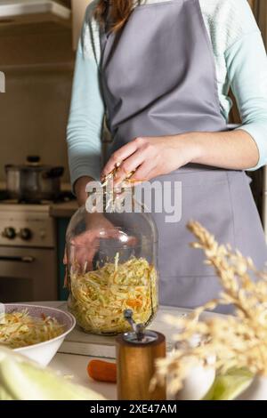 Sauerkrauteinkocherungen. Eine junge Frau bereitet in der Küche hausgemachtes Sauerkraut mit Karotten zu. Fermentierte Lebensmittel. Stockfoto