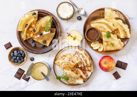 Pancake Day feiern, gesundes Frühstück. Hausgemachte süße Crepes mit Heidelbeeren, Ricotta, Äpfeln, Bananen und Schokolade auf A Stockfoto