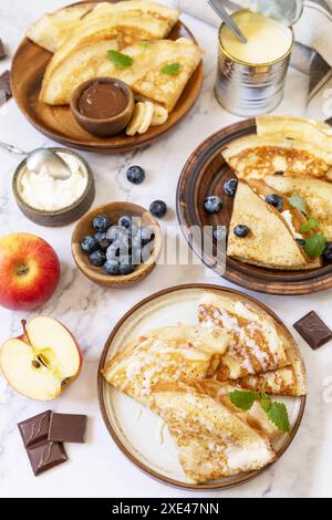 Pancake Day feiern, gesundes Frühstück. Hausgemachte süße Crepes mit Heidelbeeren, Ricotta, Äpfeln, Bananen und Schokolade auf A Stockfoto