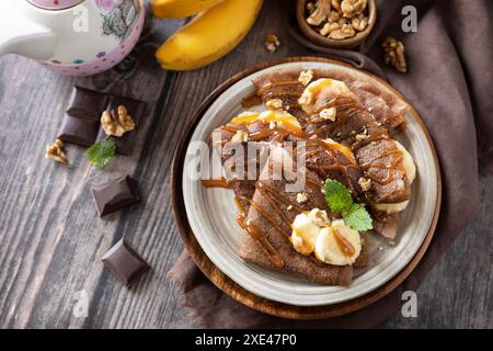 Pancake Day feiern, gesundes Frühstück. Köstliche hausgemachte Schokoladen-Crepes mit Nüssen, Karamell, Bananen auf rustikaler Holztabelle Stockfoto