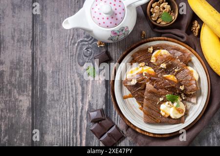 Pancake Day feiern, gesundes Frühstück. Köstliche hausgemachte Schokoladen-Crepes mit Nüssen, Karamell, Bananen auf rustikaler Holztabelle Stockfoto