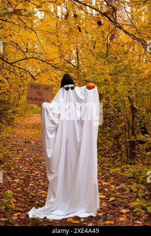 Geisterhalterkarton mit Text BRINGT MICH ZU HALLOWEEN und Kürbis trendige halloween-Feier draußen im Herbst. Handgefertigtes Geisterkostüm aus Laken, Mütze und Brille. Herbstliche Waldorange Blätter. Stockfoto