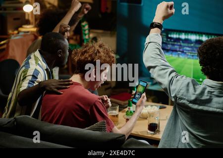 Eine Gruppe von multiethnischen, fröhlichen Fußballfans genießt am späten Abend Spiele-Livestream im Fernsehen Stockfoto