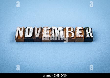 NOVEMBER. Hölzerne Buchstabenblöcke auf blau strukturiertem Hintergrund. Stockfoto