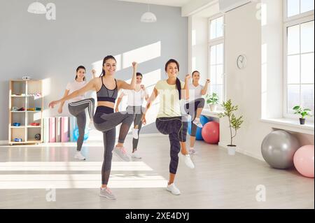 Gruppe junger sportlicher Mädchen, Frauen, die Knie bis Ellbogen Strecken, Aufwärmen mit Trainer Stockfoto