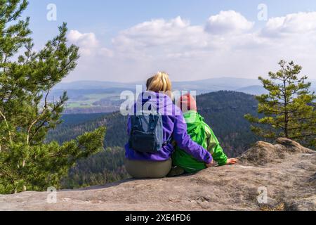 Eine junge Mutter und ihr kleiner Sohn sitzen auf einem Felsen und genießen die wunderschöne Berglandschaft. Rückansicht. Nationalpark Sächsische Schweiz in der Nähe Stockfoto