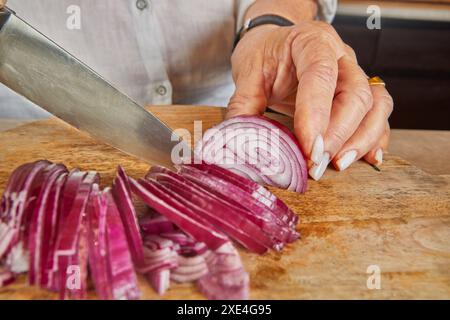 Eine Frau schneidet lila Zwiebeln auf einem Holzbrett in ihrer Küche. Stockfoto