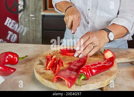 Detaillierte kulinarische Vorbereitung Frau, die frische rote Paprika auf einem Holzbrett in einer Küche schneidet. Stockfoto