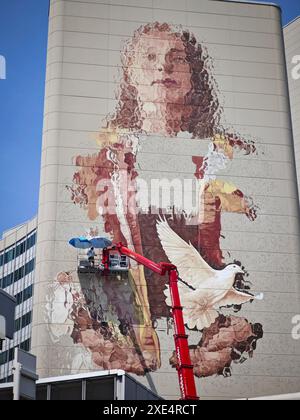 Wien, Österreich. Juni 2024. Die australische Künstlerin Fintan Magee malt eine weibliche Figur mit einer Taube an einer Wand des Vienna International Center (VIC) in luftiger Höhe. In Zusammenarbeit mit dem Wiener Kulturverein Calle Libre, den UN-Organisationen in Wien und weiteren Projektpartnern entsteht Wiens größtes Wandbild. Sie dient der Unterstützung der Nachhaltigkeitsziele und des künftigen UN-Gipfels im September. Frank Rumpenhorst/dpa/Alamy Live News Stockfoto