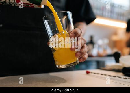 Nahaufnahme eines nicht erkennbaren Barkepers, der Saft in ein mit alkoholischem Getränk gefülltes Glas gießt. Nahaufnahme von alkoholfreien Getränken mit Orangengeschmack in Glas Stockfoto