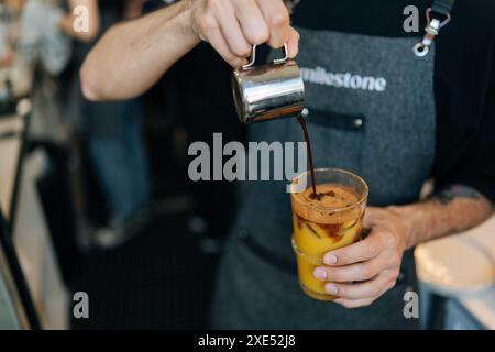 Zugeschnittene Aufnahme eines nicht erkennbaren Barista-Mannes, der Eiskaffee mit frischem Orangensaft im Glas zubereitet. Nahaufnahme der Kellnerin im Café, die Kaffee serviert Stockfoto