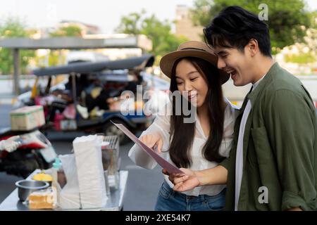 Asiatische Paarreisender mit lässiger Kleidung und Hut in Beziehung kaufte einen Dessertsnack am Abend auf dem Street Food Markt. Backpacker reisen in Bangkok, Thailand. Stockfoto
