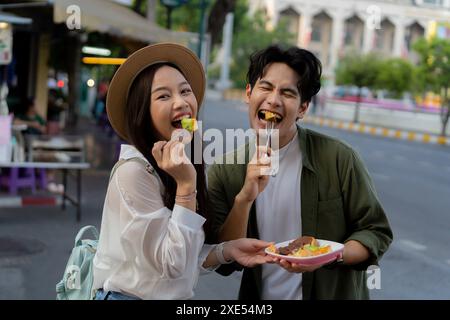 Asiatische Paarreisender mit lässiger Kleidung und Hut in Beziehung kaufte einen Dessertsnack am Abend auf dem Street Food Markt. Backpacker reisen in Bangkok, Thailand. Stockfoto
