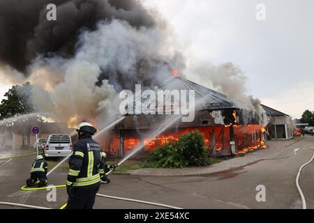 Kempten, Deutschland. Juni 2024. Feuerwehrleute arbeiten daran, ein brennendes Gebäude zu löschen. Nach dem Brand in einem ehemaligen Autohaus im Westen von Kempten schätzt die Polizei den Schaden zunächst auf einstellige Millionenbeträge. Rund 270 Feuerwehrleute, technische Hilfskräfte, Polizei und Rettungsdienste waren am Dienstagabend stundenlang im Einsatz, wie die Polizei am Mittwochabend mitteilte. Die Brandursache blieb zunächst unklar und wurde Gegenstand von Ermittlungen durch die Strafverfolgungsabteilung. Quelle: Markus Dorer/dpa/Alamy Live News Stockfoto