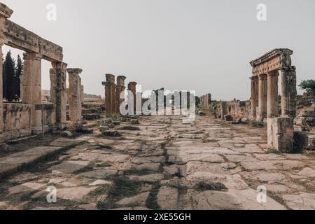 Die zerbröckelnden Ruinen und Säulen der Frontinus-Straße in der Nähe des Frontinus-Tores in der alten Ruinenstadt Hierapolis in Türkiye an einem hellen sonnigen Tag. Stockfoto