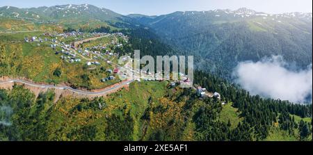 Aus der Vogelperspektive die gewundene Bergstraße führt zum malerischen Dorf Gomismta, Georgia, eingebettet in üppige Wälder und umgeben von dichten Nebelschichten oder Wolken, die die ruhige und abgeschiedene alpine Landschaft betonen. Stockfoto