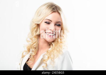 Blonde Frau mit lockigem Haar, eine weiße Jacke, lacht mit geschlossenen Augen. Ihr breites Lächeln und die sichtbaren Zähne strahlen Glück und Wärme aus, c Stockfoto