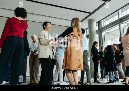 Frauen grüßen sich bei einer Büroveranstaltung, während sich andere Kollegen im Hintergrund mischen und eine lebendige und gesellige Atmosphäre schaffen. Stockfoto