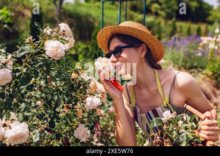 Porträt einer jungen Gärtnerin, die nach Strauchpflege im Sommergarten Krokusrosen riecht. Genießen Sie weiße Blüten nach dem Deadhead Stockfoto