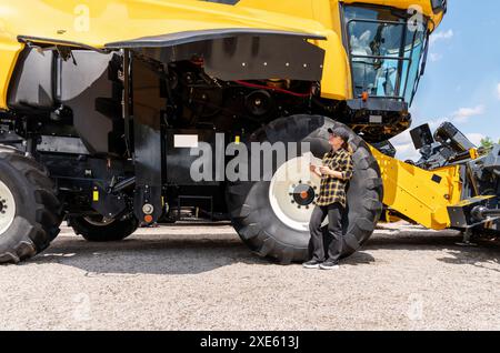 Eine Landwirtin mit einem digitalen Tablet steht neben einem Mähdrescher in einem Landmaschinenbetrieb. Stockfoto