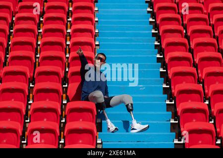 Behinderte Athleten in einem blauen Shirt sitzen auf den roten Sitzen im Stadion und bereiten sich auf das Lauftraining vor. Stockfoto